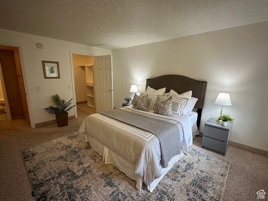 Bedroom with carpet floors, a textured ceiling, baseboards, and a walk in closet