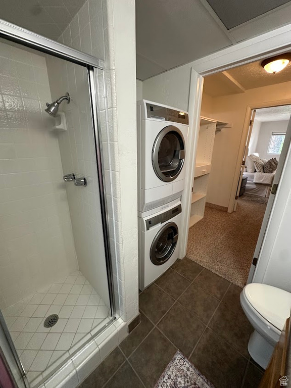 Full bath with stacked washing machine and dryer, a stall shower, tile patterned floors, and toilet