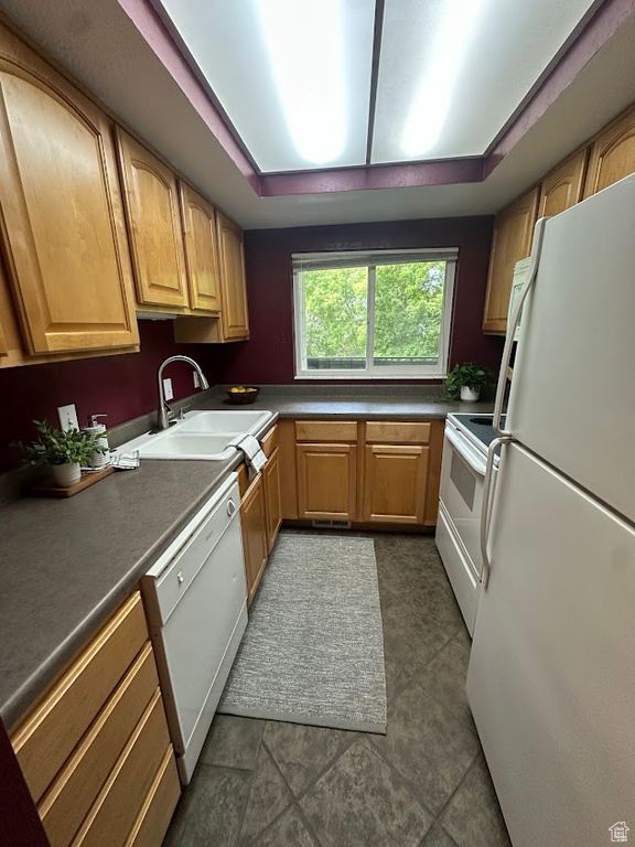 Kitchen featuring white appliances, a sink, dark countertops, and dark tile patterned floors