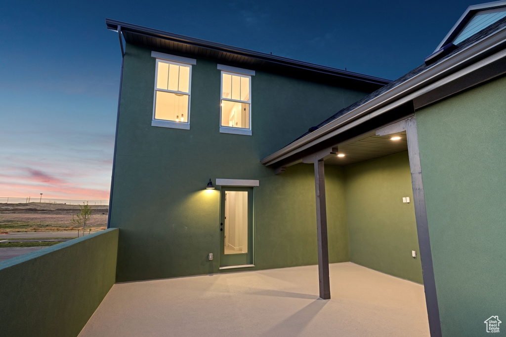 Back of house at dusk with stucco siding and a balcony