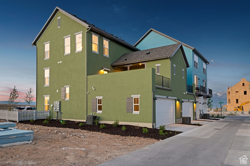 Property exterior at dusk with stucco siding, a garage, driveway, and central AC
