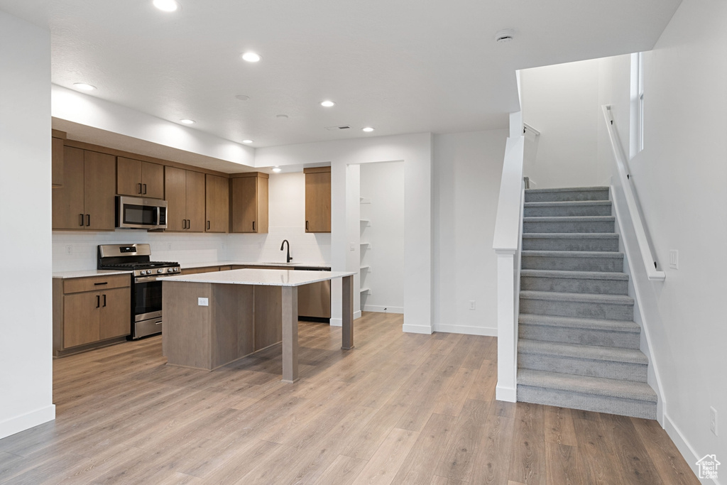 Kitchen featuring appliances with stainless steel finishes, a sink, baseboards, light wood-type flooring, and light countertops