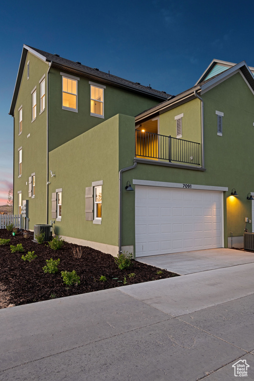 View of front of property with stucco siding, an attached garage, driveway, a balcony, and central AC unit