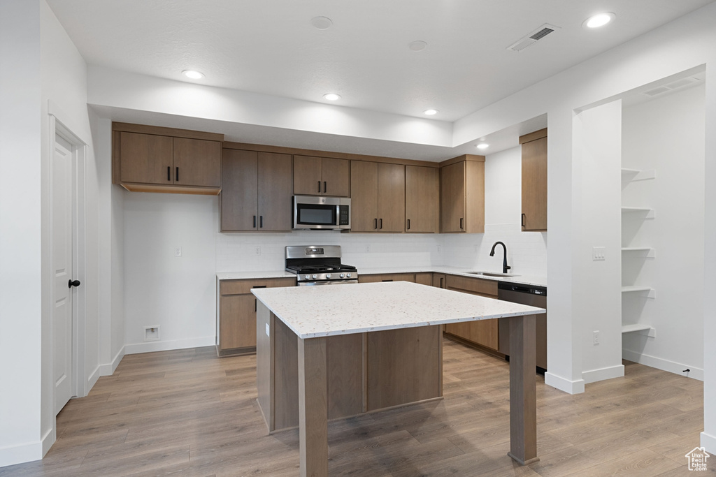 Kitchen with appliances with stainless steel finishes, a sink, a center island, backsplash, and light wood finished floors