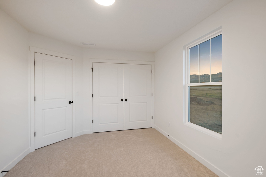 Unfurnished bedroom with light colored carpet, baseboards, and a closet