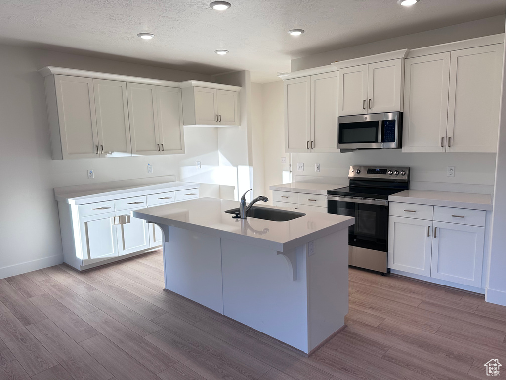 Kitchen featuring appliances with stainless steel finishes, white cabinetry, sink, a kitchen island with sink, and light hardwood / wood-style flooring
