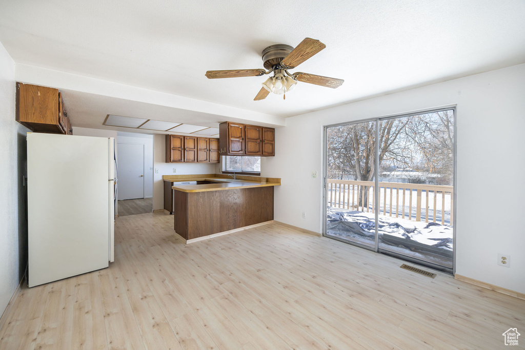 Kitchen with kitchen peninsula, white refrigerator, light hardwood / wood-style floors, and ceiling fan