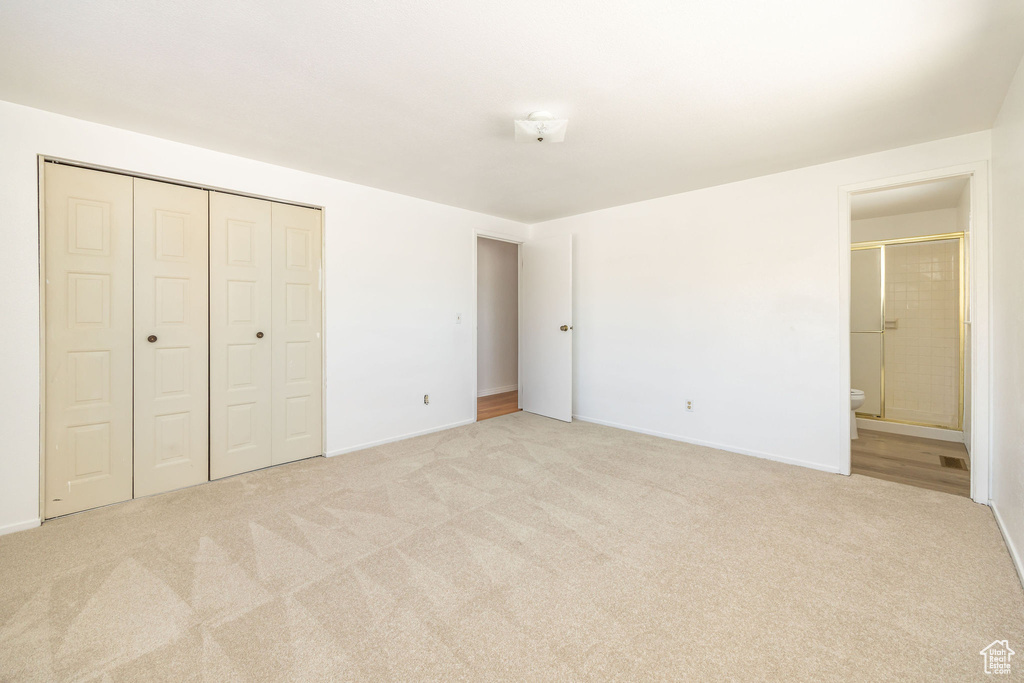 Unfurnished bedroom featuring light colored carpet, ensuite bathroom, and a closet