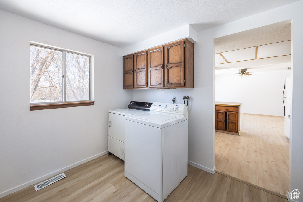 Laundry room featuring light wood-type flooring, ceiling fan, washer and clothes dryer, and cabinets