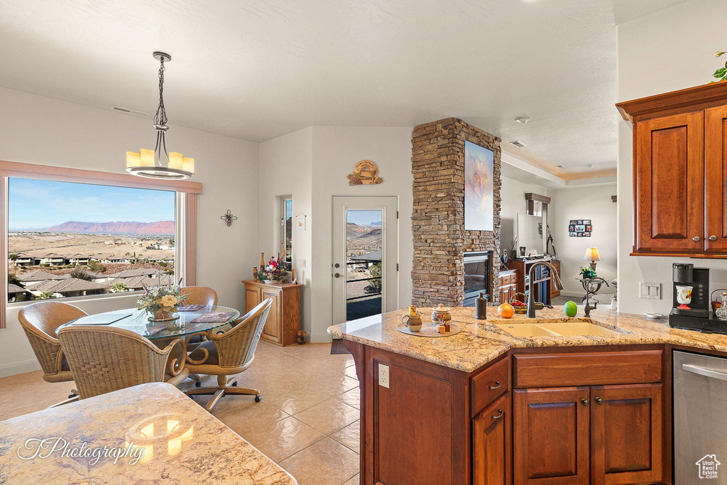 Kitchen featuring dishwasher, hanging light fixtures, sink, a stone fireplace, and light stone counters