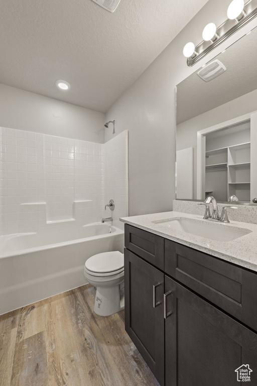 Full bathroom with hardwood / wood-style floors, a textured ceiling, shower / tub combination, toilet, and vanity