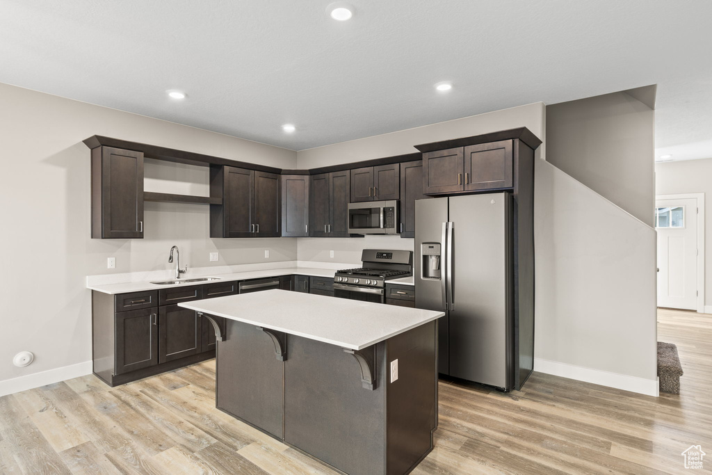 Kitchen with dark brown cabinetry, appliances with stainless steel finishes, a kitchen island, a kitchen bar, and sink