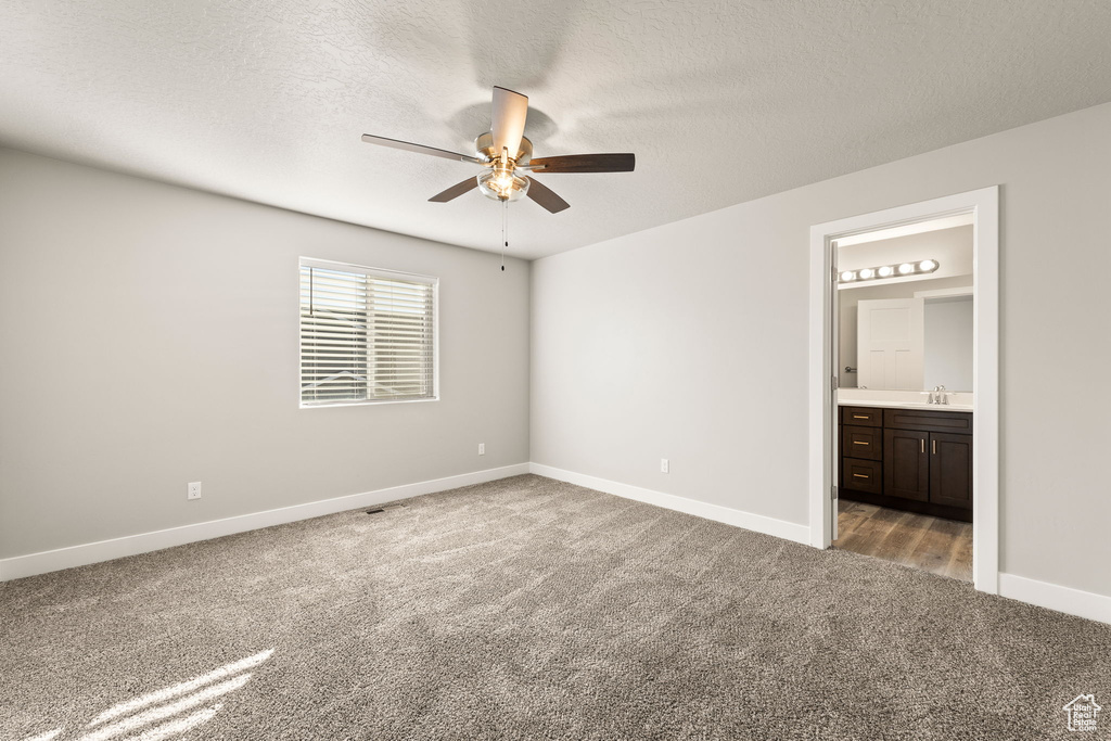 Unfurnished bedroom featuring ceiling fan, ensuite bathroom, a textured ceiling, and light carpet