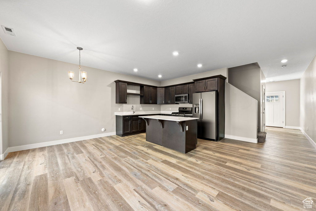 Kitchen with a kitchen breakfast bar, dark brown cabinets, decorative light fixtures, an inviting chandelier, and stainless steel appliances