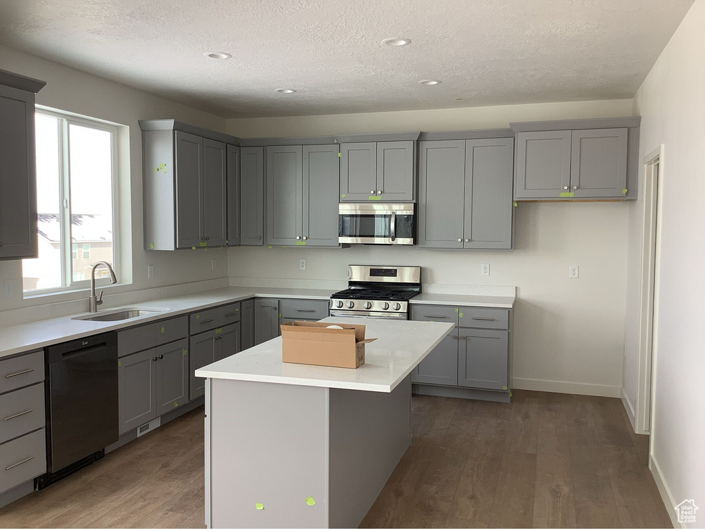 Kitchen with gray cabinetry, dark wood finished floors, light countertops, appliances with stainless steel finishes, and a sink