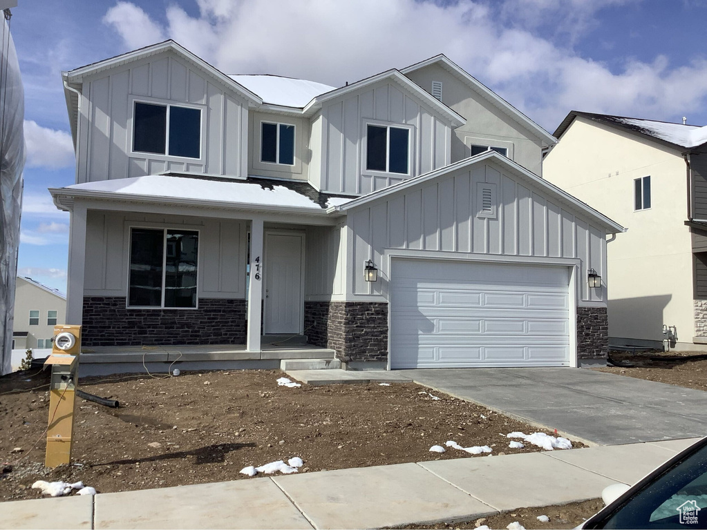 View of front of home featuring driveway, covered porch, board and batten siding, and stone siding