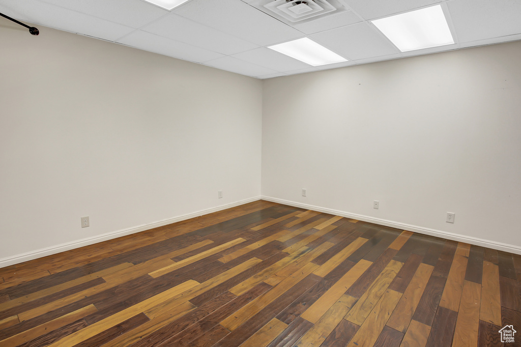 Empty room with a drop ceiling and dark hardwood / wood-style flooring