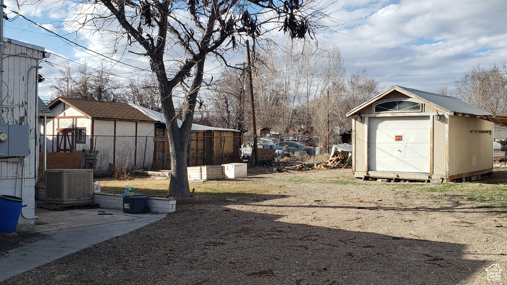 View of yard featuring a storage shed, an outdoor structure, fence, and central AC