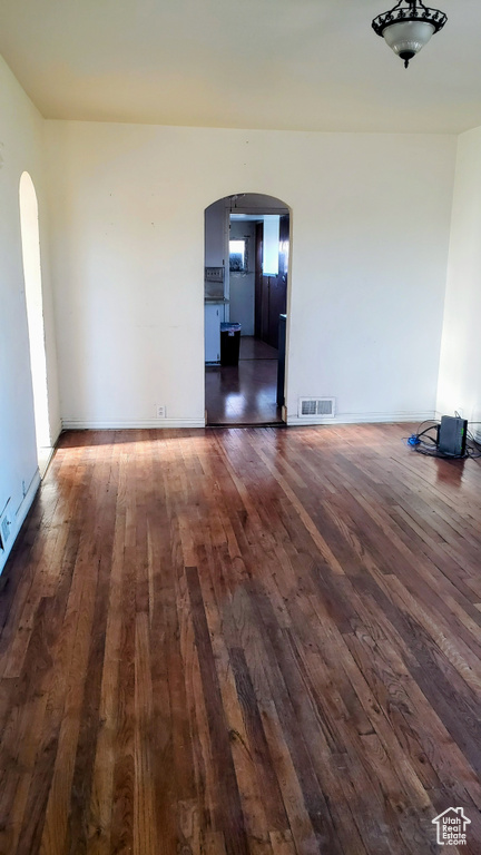 Empty room with arched walkways, dark wood-type flooring, and baseboards