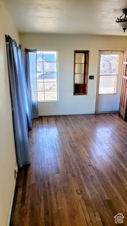 Unfurnished living room featuring dark wood-type flooring, a textured ceiling, and baseboards