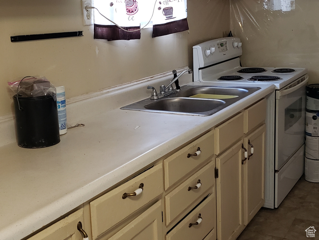 Kitchen with white range with electric cooktop, cream cabinets, and sink