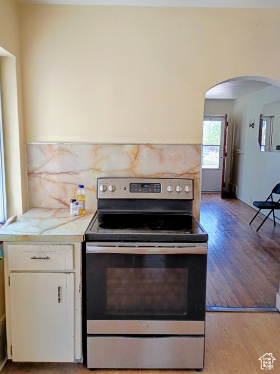 Kitchen with stainless steel range with electric cooktop, arched walkways, light countertops, white cabinetry, and light wood-type flooring