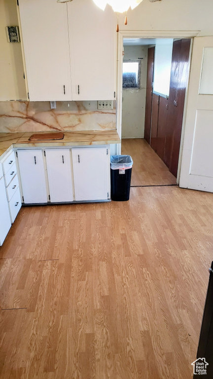 Kitchen with light wood finished floors, light countertops, white cabinets, and backsplash