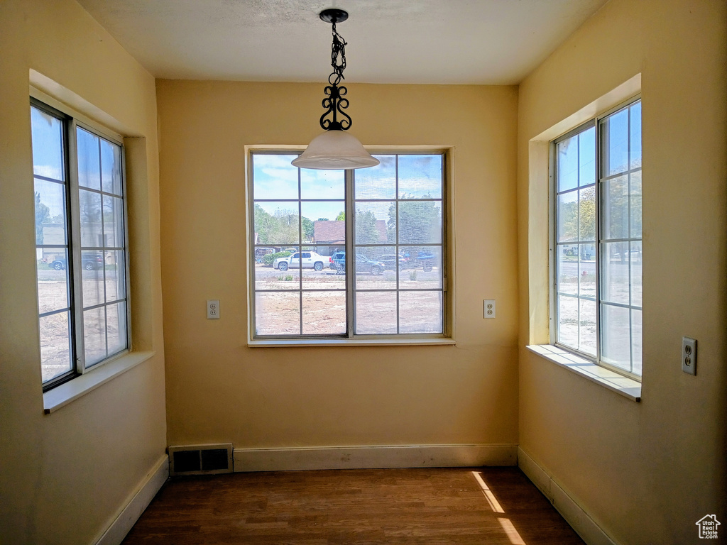 Unfurnished dining area featuring dark wood-type flooring and baseboards