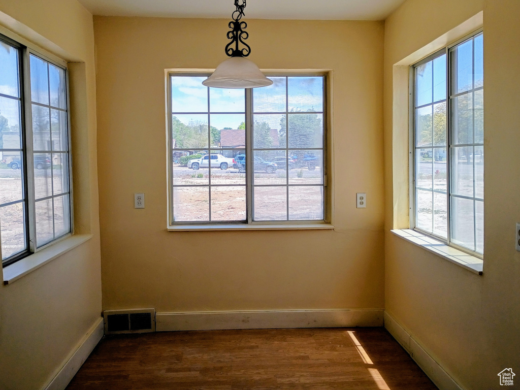 Unfurnished dining area featuring dark wood-type flooring and baseboards