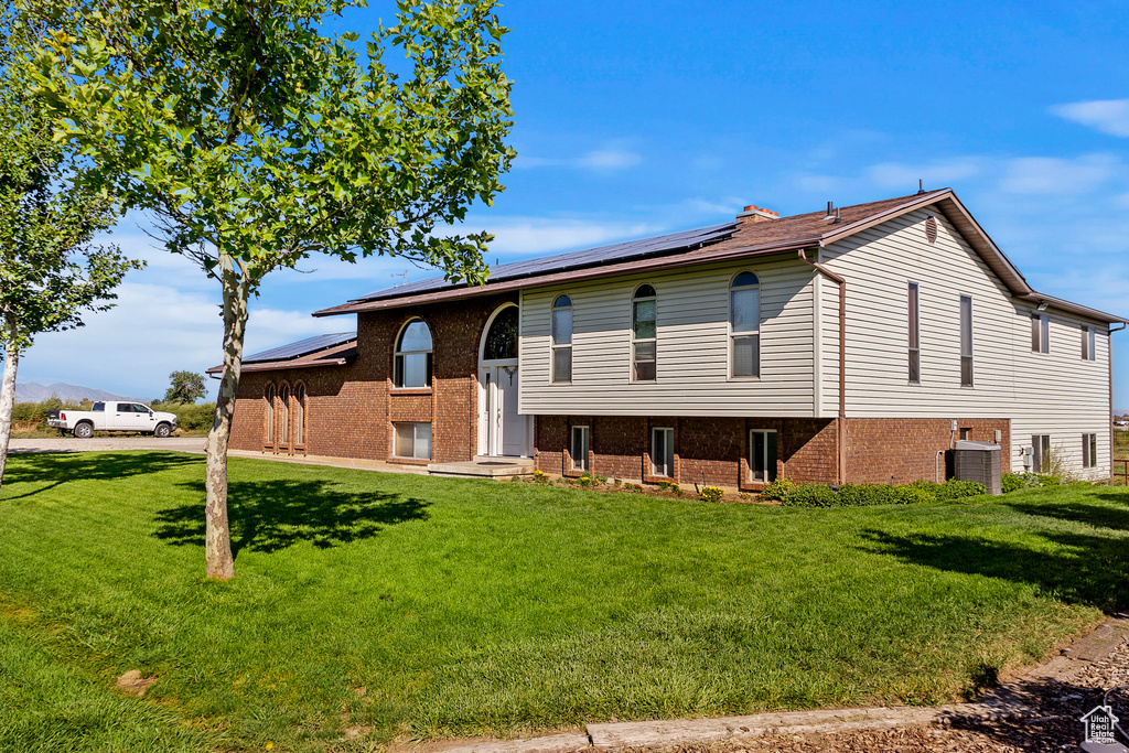Raised ranch featuring central AC, solar panels, and a front lawn