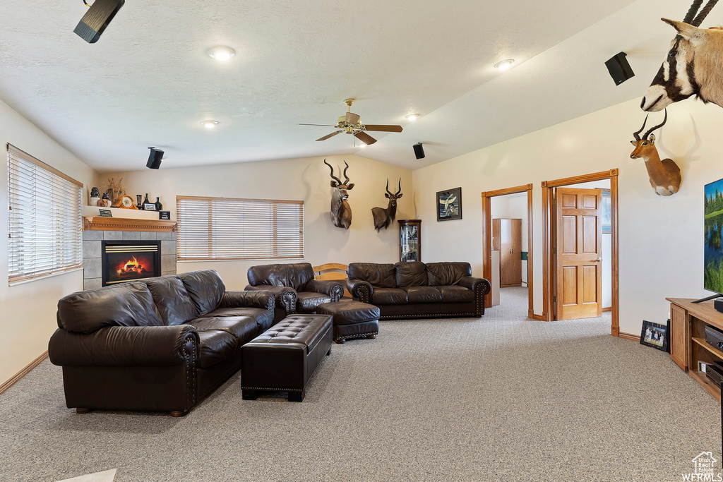 Living room with ceiling fan, carpet, a tiled fireplace, and lofted ceiling
