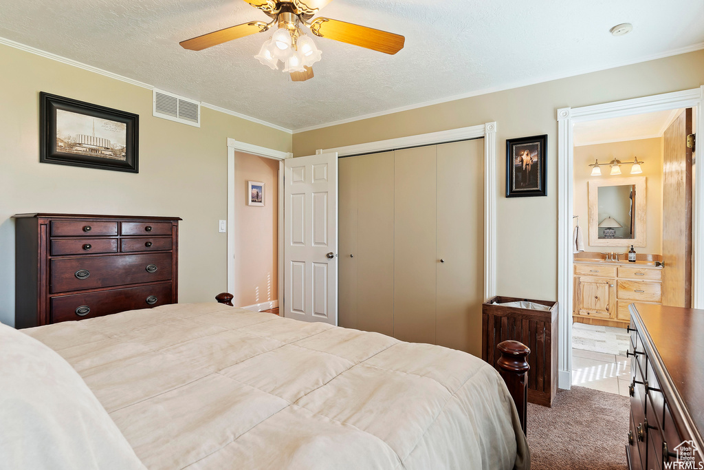 Carpeted bedroom featuring ceiling fan, a textured ceiling, ornamental molding, and ensuite bath