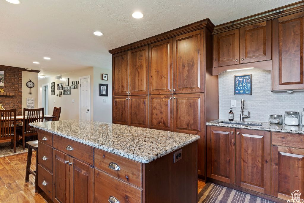 Kitchen featuring hardwood / wood-style floors, light stone countertops, sink, a kitchen island, and backsplash