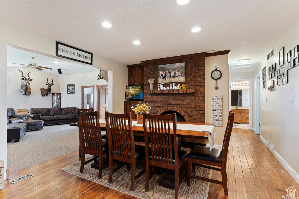 Dining room with a fireplace, ceiling fan, and light wood-type flooring