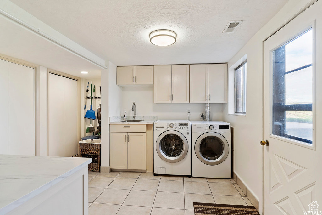 Washroom with a textured ceiling, sink, washing machine and dryer, cabinets, and light tile patterned flooring