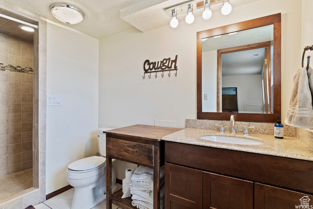 Bathroom with vanity, toilet, a tile shower, and tile patterned flooring