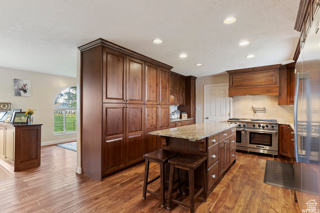 Kitchen featuring appliances with stainless steel finishes, a kitchen island, dark wood-type flooring, backsplash, and light stone counters
