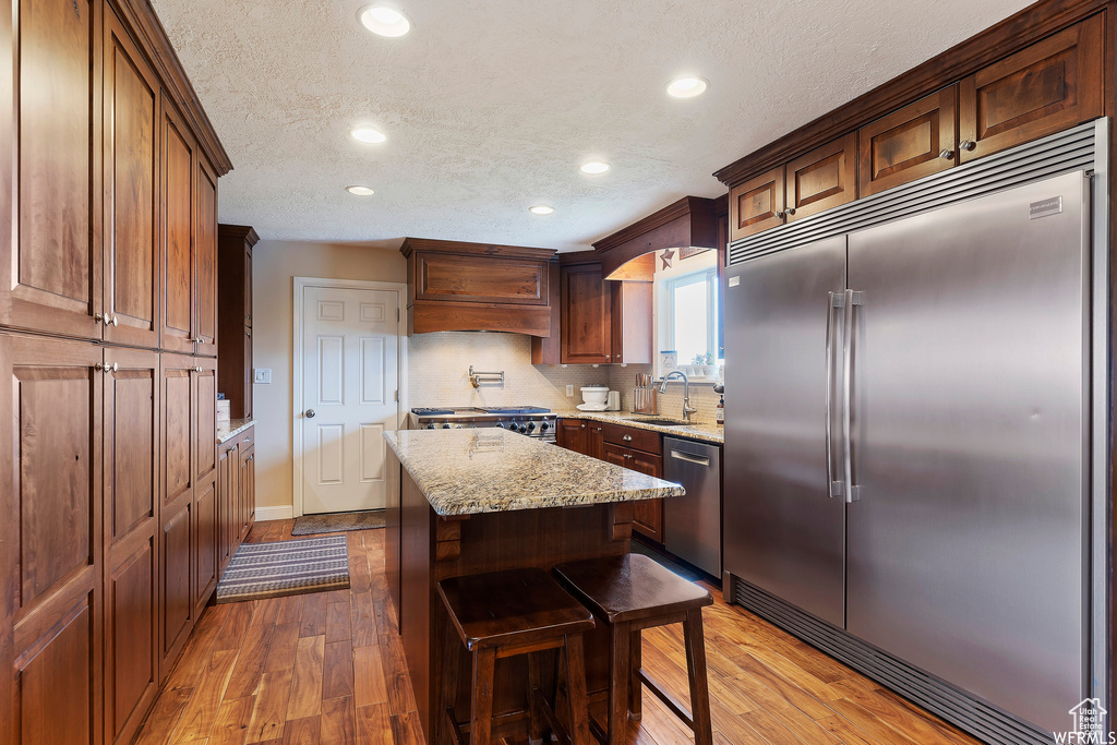 Kitchen featuring appliances with stainless steel finishes, sink, custom exhaust hood, tasteful backsplash, and a kitchen island