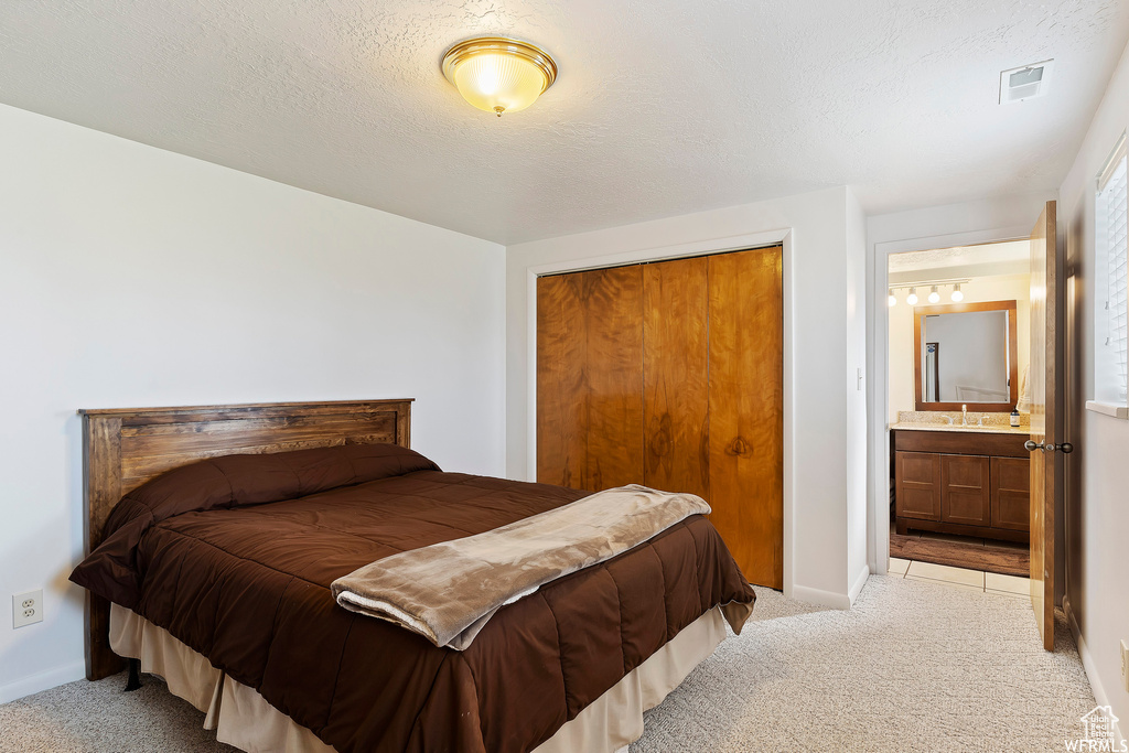 Carpeted bedroom featuring a closet, connected bathroom, and a textured ceiling