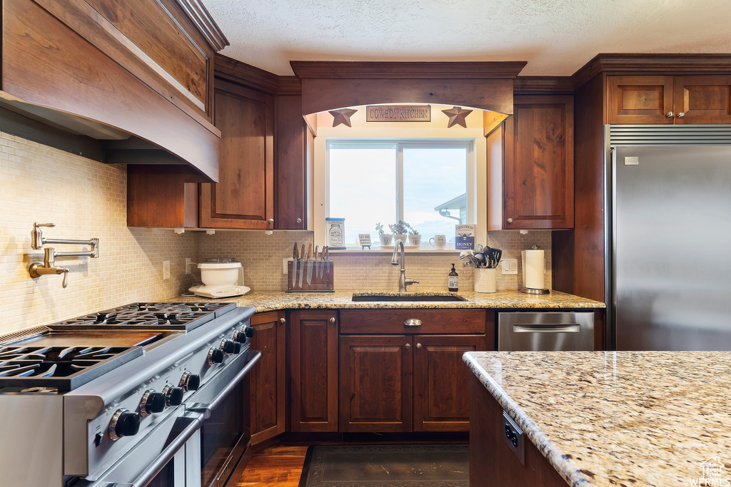 Kitchen with sink, dark wood-type flooring, backsplash, stainless steel appliances, and light stone counters