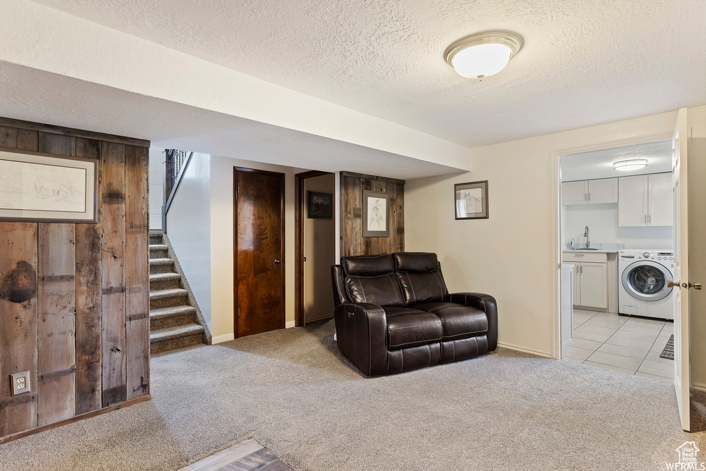 Living room with a textured ceiling, washer / clothes dryer, light carpet, sink, and wood walls