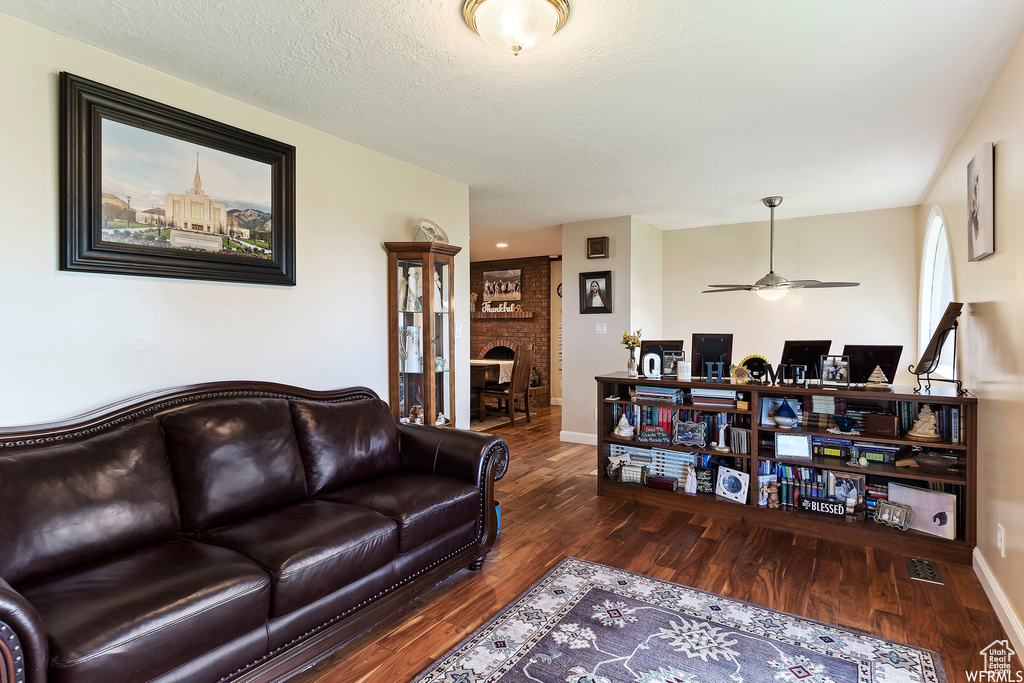 Living room featuring ceiling fan, a brick fireplace, and dark hardwood / wood-style floors