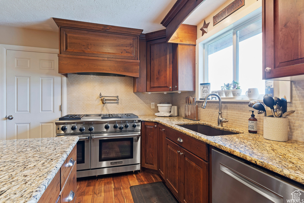 Kitchen featuring sink, premium range hood, backsplash, light stone counters, and stainless steel appliances