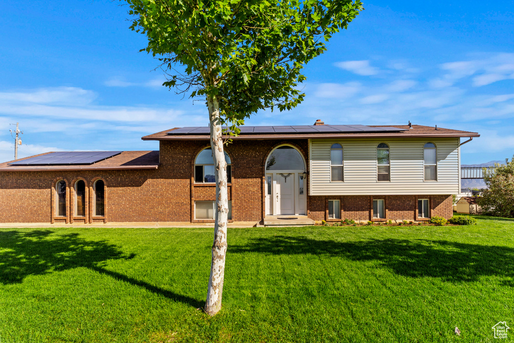 Raised ranch featuring a front lawn and solar panels