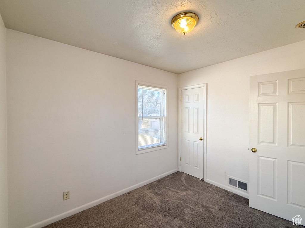 Unfurnished room with dark colored carpet and a textured ceiling