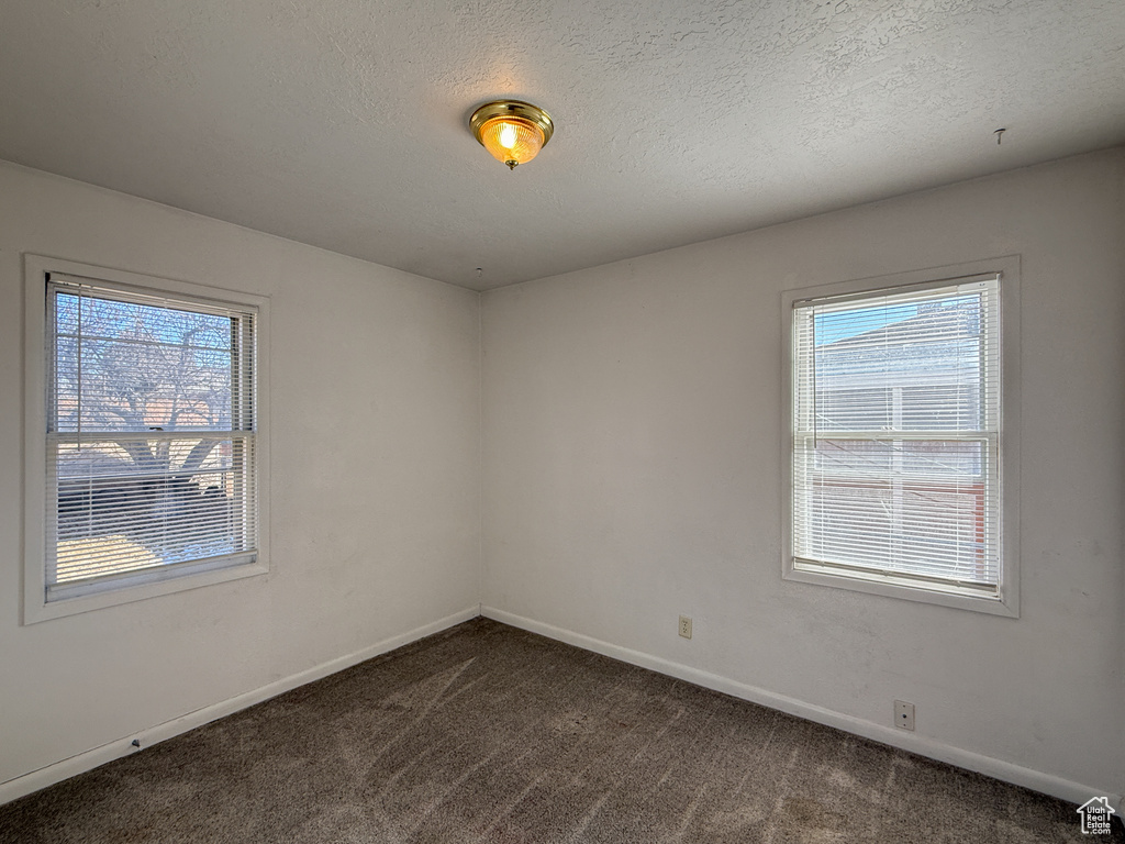Spare room featuring dark colored carpet, plenty of natural light, and a textured ceiling