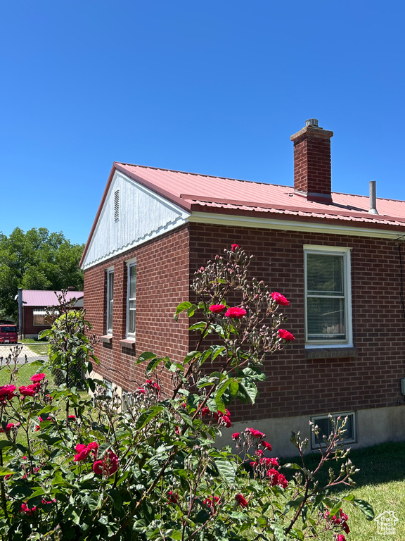 View of property exterior with brick siding, a chimney, and metal roof