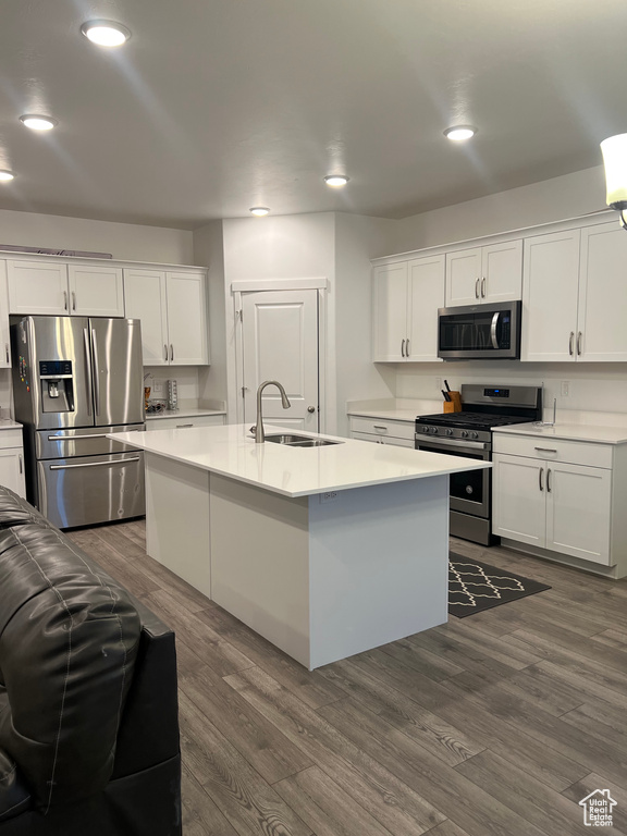 Kitchen with appliances with stainless steel finishes, sink, white cabinets, dark wood-type flooring, and an island with sink
