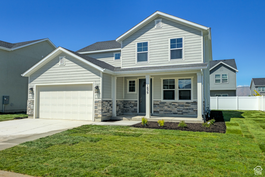 View of front facade featuring covered porch, an attached garage, driveway, and stone siding