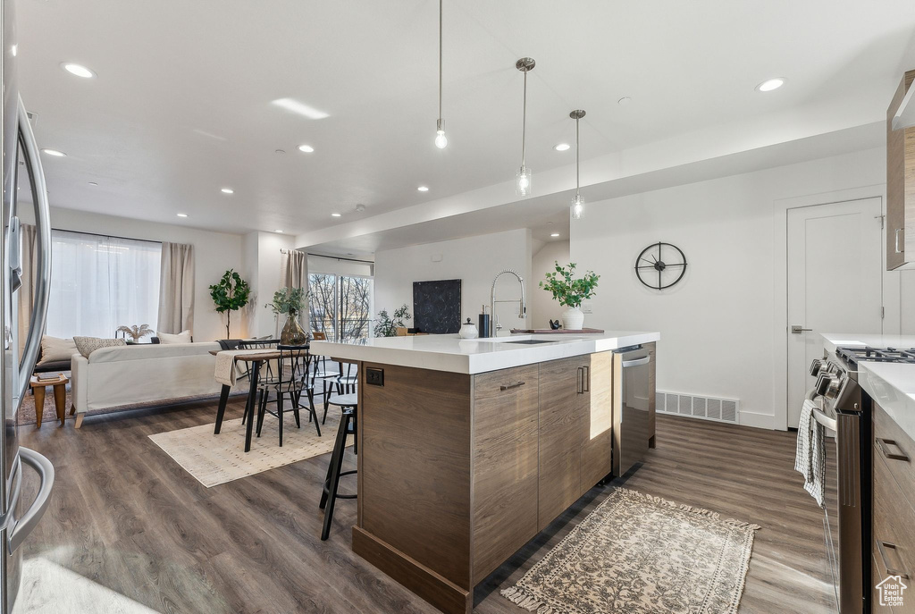 Kitchen with dark wood-type flooring, appliances with stainless steel finishes, sink, and a kitchen island with sink